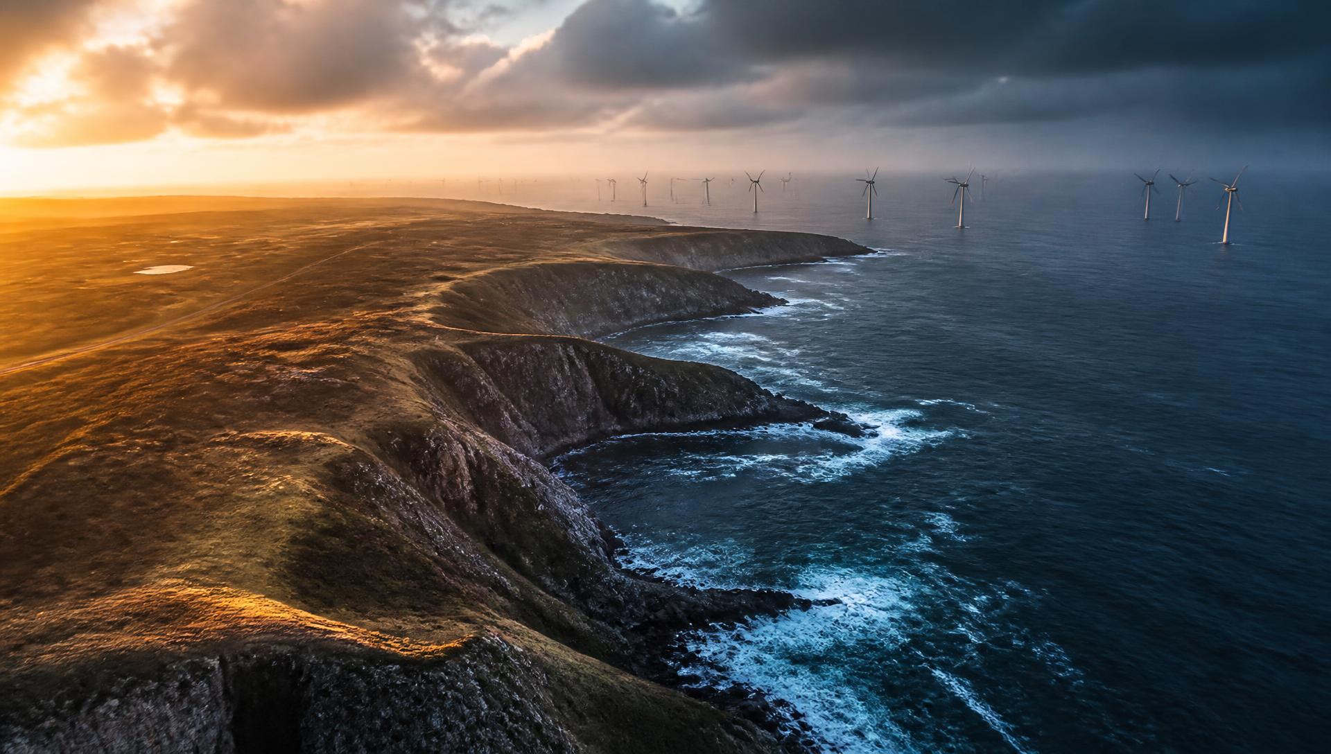 Aerial drone view of a coastline with offshore wind turbines at sunrise